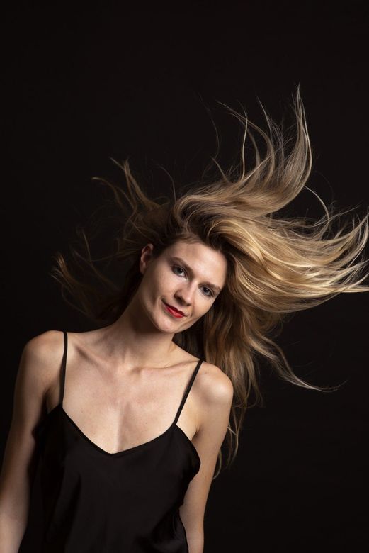 Retrato de una mujer rubia que se mueve al ritmo de la música sobre un fondo oscuro, vestida con una blusa negra.