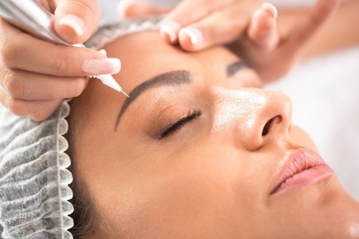 Esteticista aplicando un tratamiento de cejas a una clienta recostada en un entorno de spa.