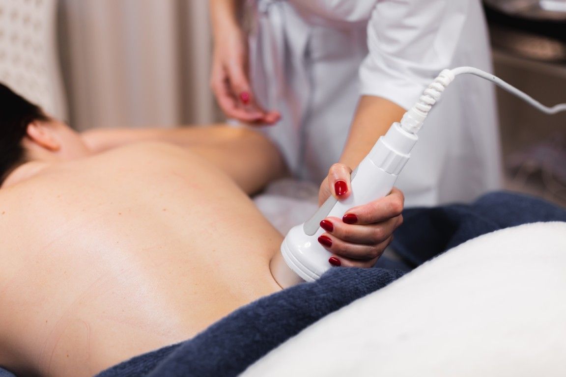 Terapeuta utilizando un dispositivo de masaje manual en la espalda desnuda de una persona en una sala de tratamientos de spa.
