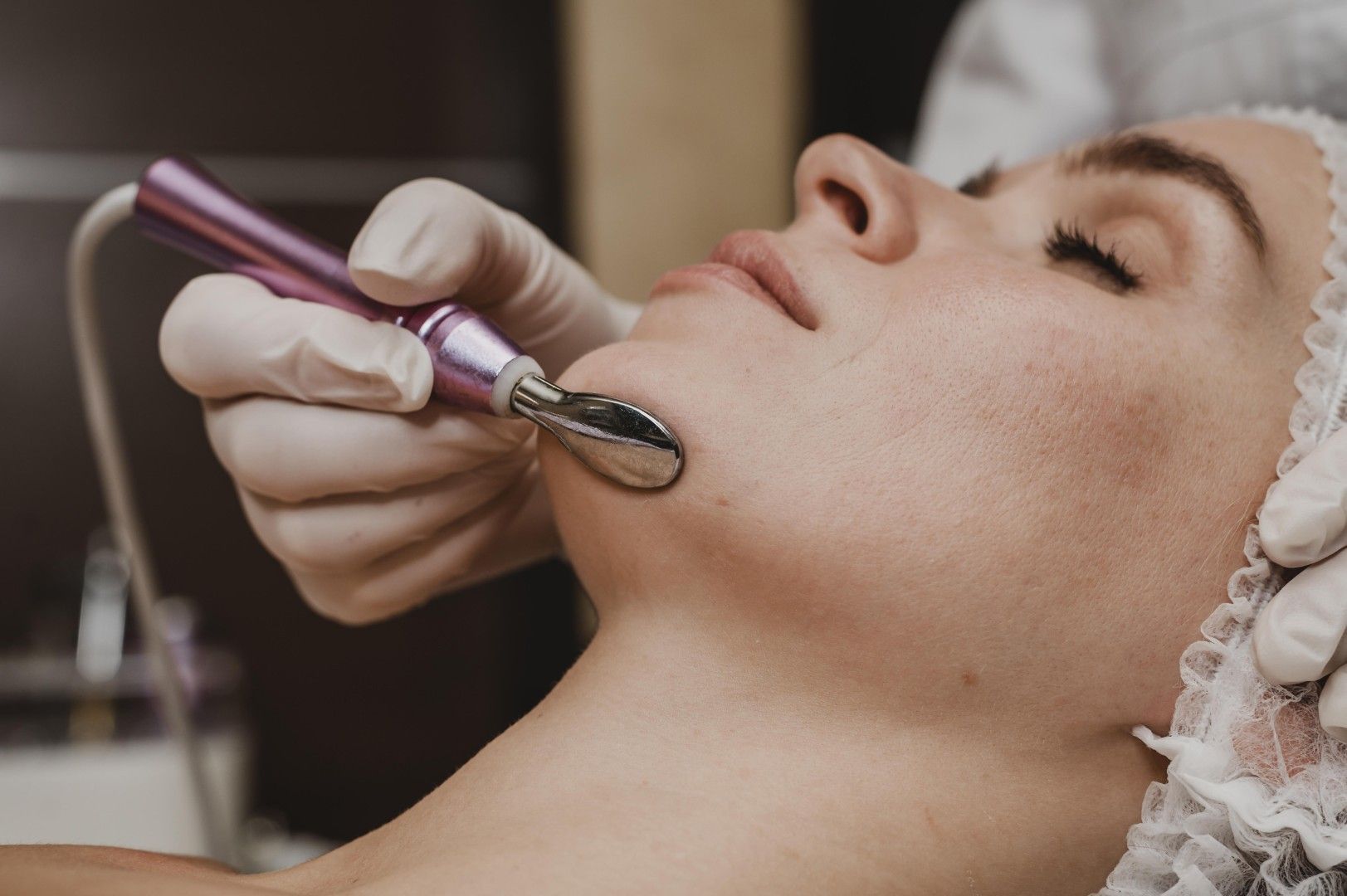 Un tratamiento facial realizado con una mano enguantada que utiliza un dispositivo para el cuidado de la piel.