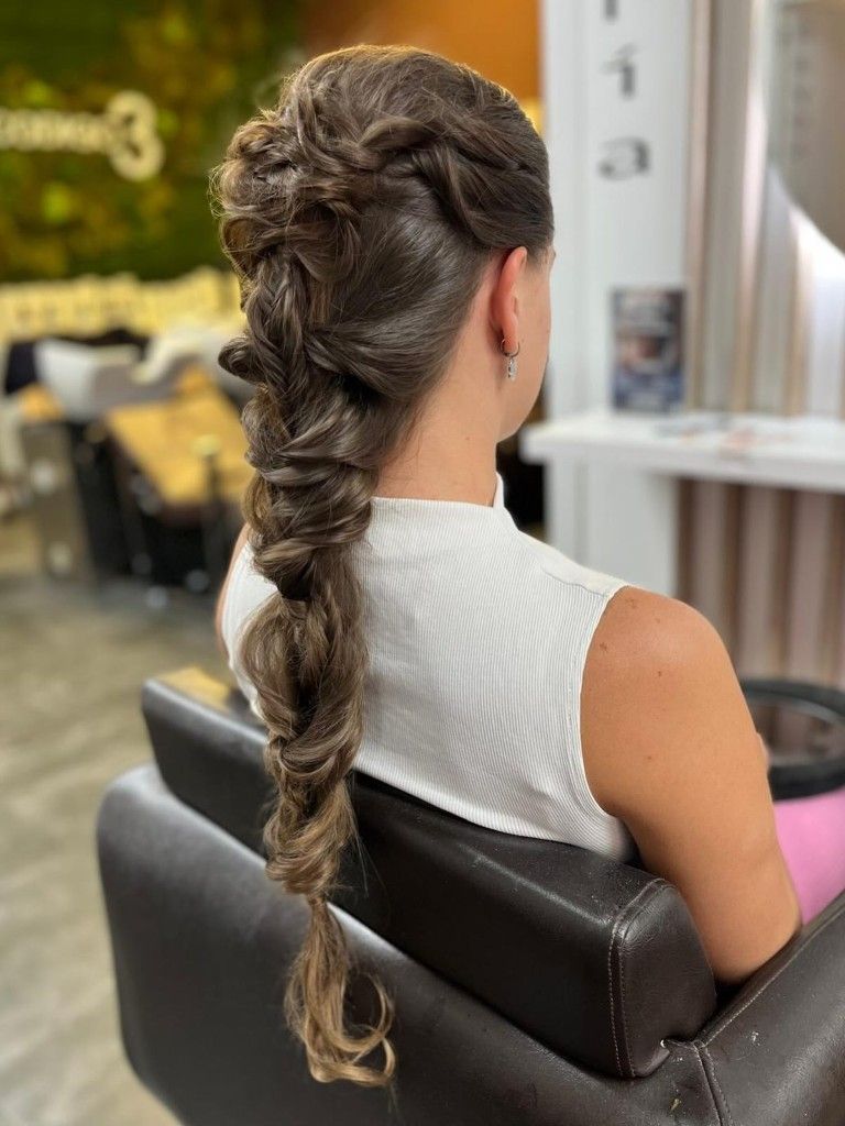 Mujer con el pelo largo trenzado sentada en una silla de peluquería, vista desde atrás.