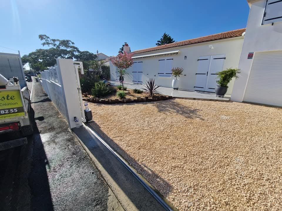 Une maison blanche moderne avec des volets bleus, une allée de gravier et des parterres de jardin aménagés derrière une clôture contemporaine.