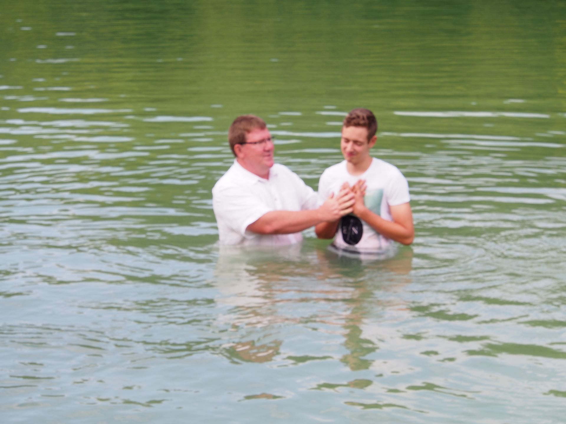 Ein Mann tauft einen anderen Mann in einem See.