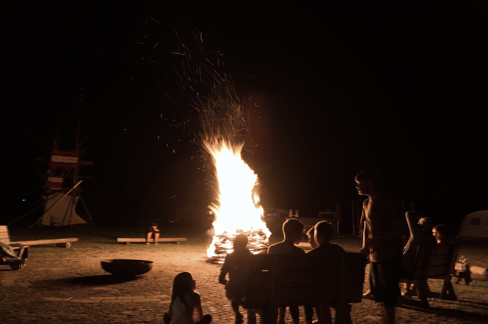 Eine Gruppe von Menschen sitzt nachts um ein Lagerfeuer herum.