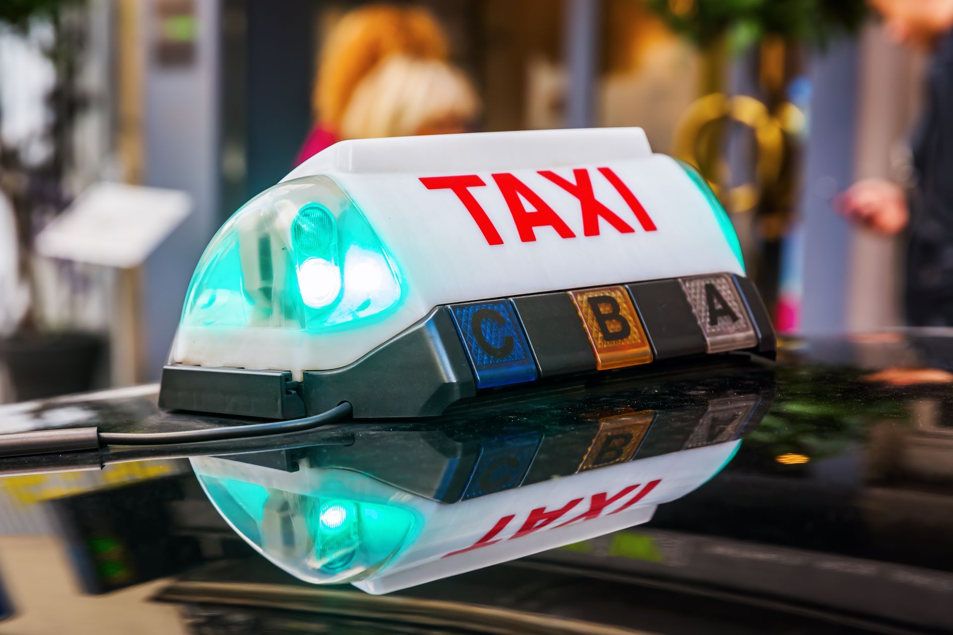 Feu de taxi sur le toit de la voiture avec indicateur vert lumineux et panneau TAXI rouge reflétés sur une surface brillante