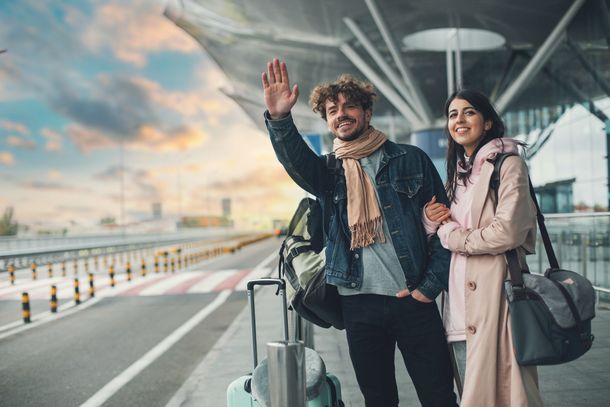 Deux voyageurs avec des bagages font signe à un terminal de l'aéroport.