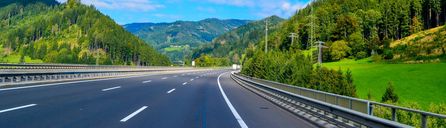 Autoroute déserte serpentant à travers des montagnes verdoyantes sous un ciel d'un bleu limpide