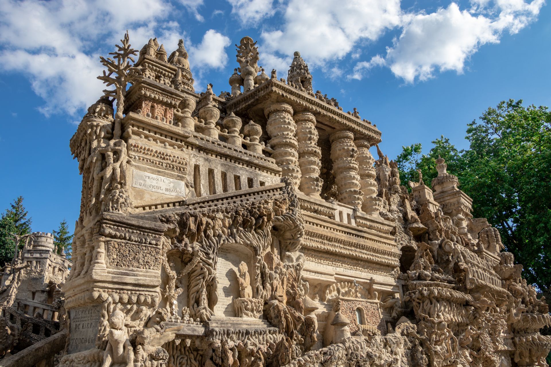 Temple en pierre finement sculptée, aux tours ornées, se détachant sur un ciel bleu nuageux.