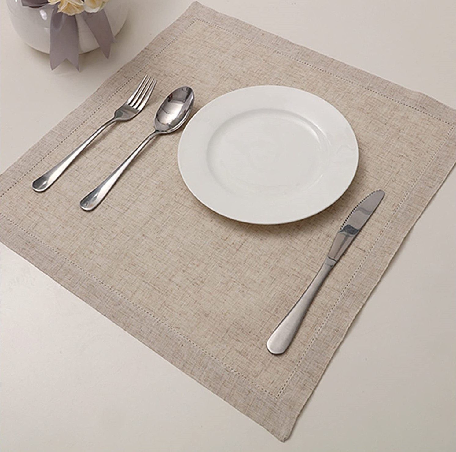 Un plato blanco con cubiertos sobre un mantel individual.