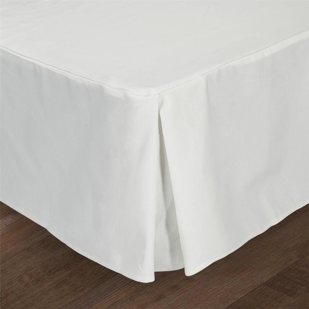 Una falda de cama blanca reposa sobre un suelo de madera.