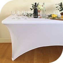 Mesa rectangular blanca con funda a medida, equipada con cristalería y bebidas.
