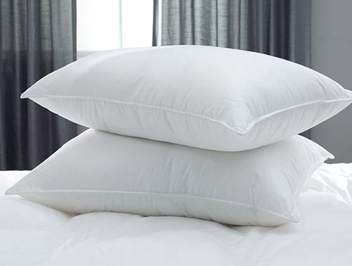 Dos almohadas blancas están apiladas una encima de otra en una cama.