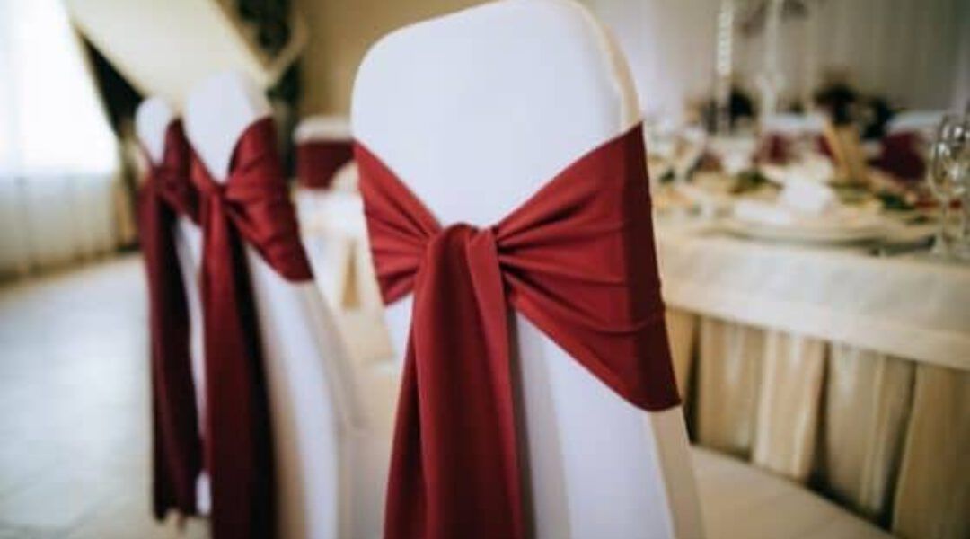 Una fila de sillas blancas con lazos rojos.