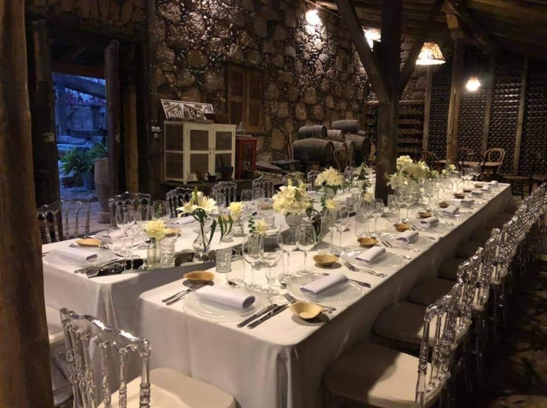 Una mesa larga con un mantel blanco y sillas transparentes está preparada para una recepción de boda.