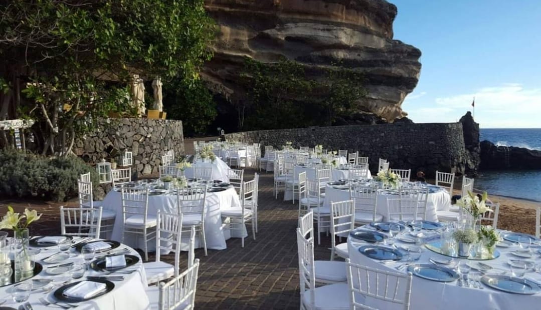 Una fila de mesas y sillas preparadas para una recepción de boda en la playa.
