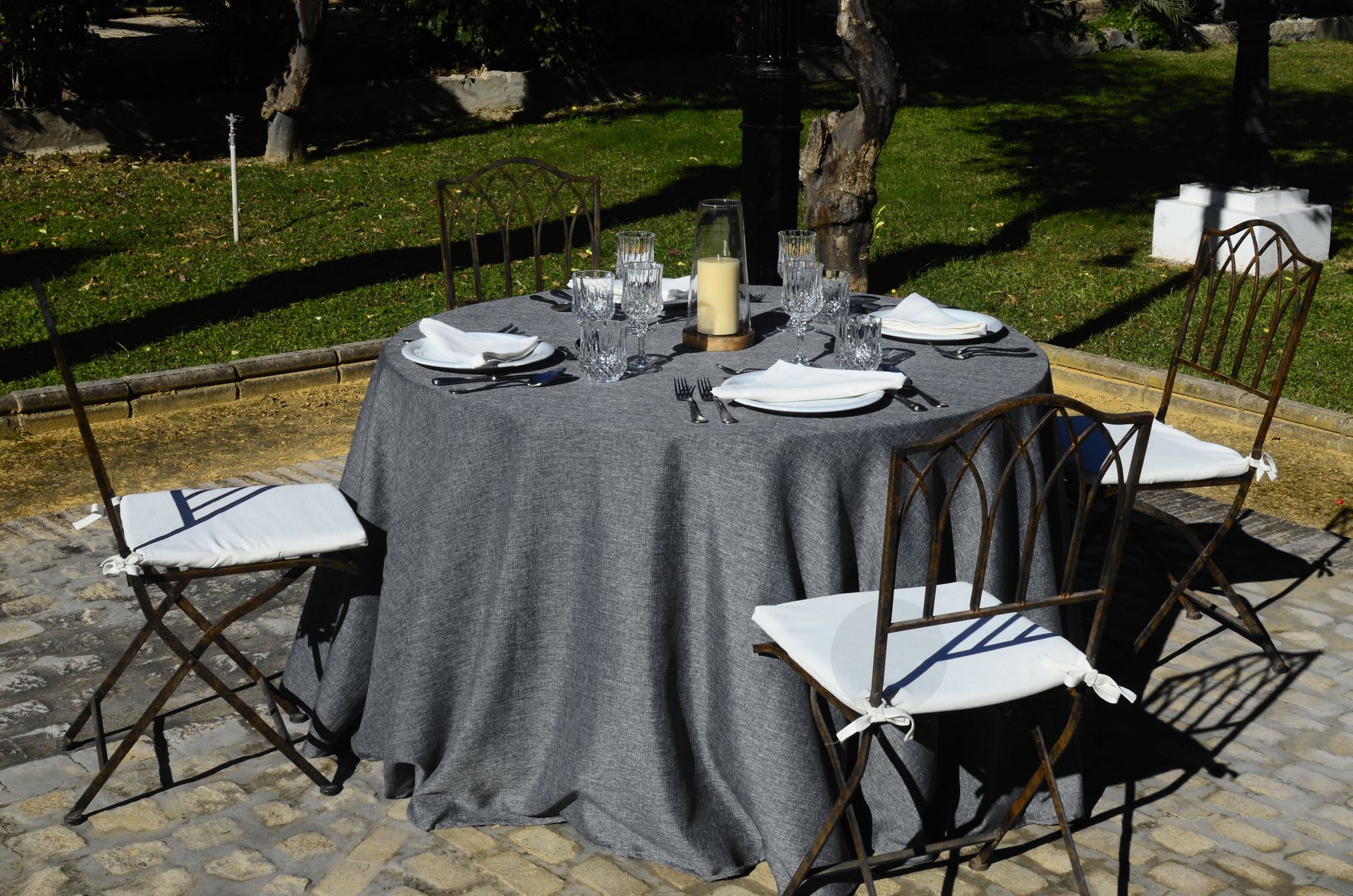 Conjunto de mesa redonda para cenar al aire libre, rodeada de sillas, con mantel gris oscuro.