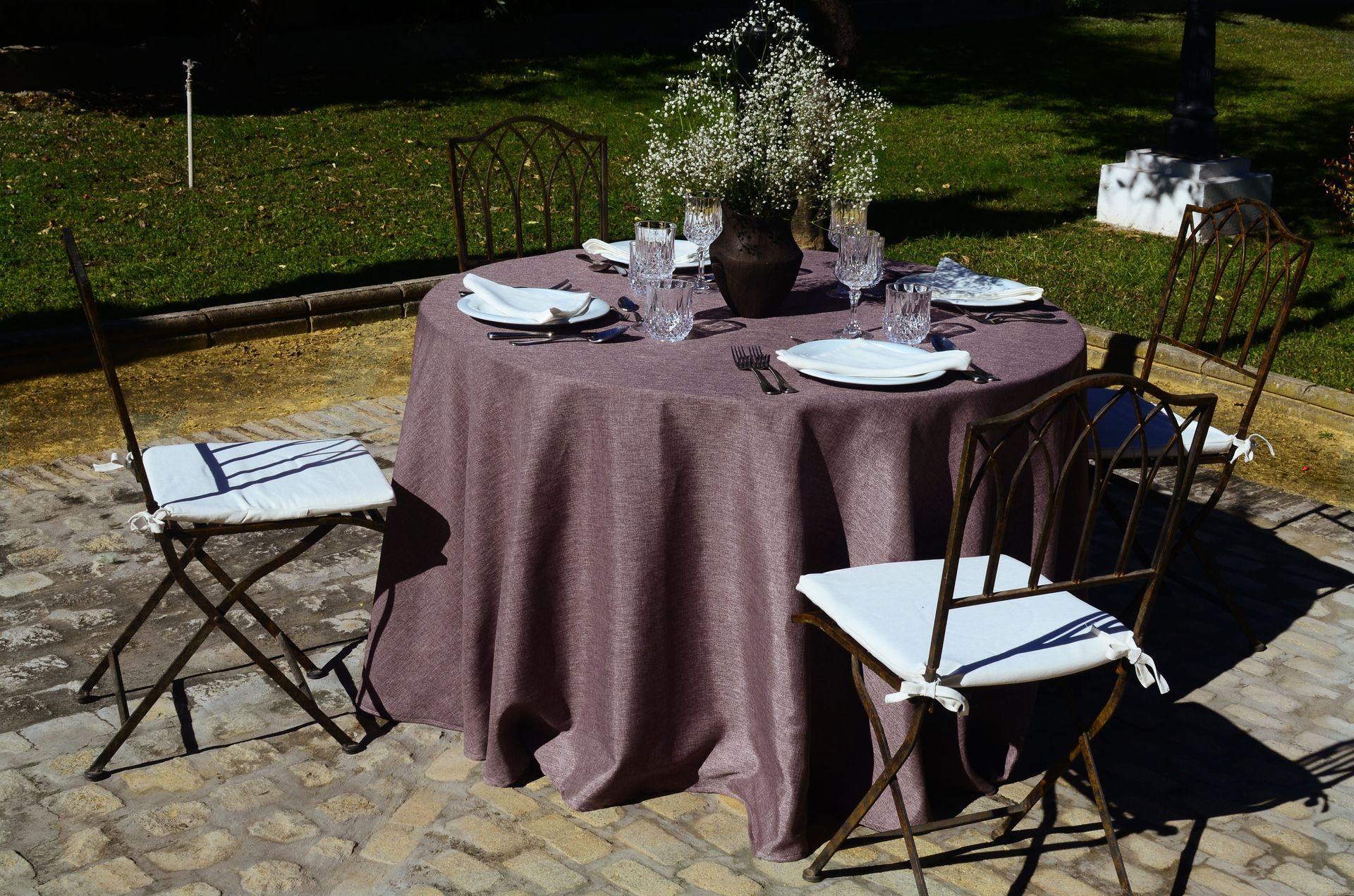 Mesa para exterior con cuatro sillas, mantel morado y arreglo floral.