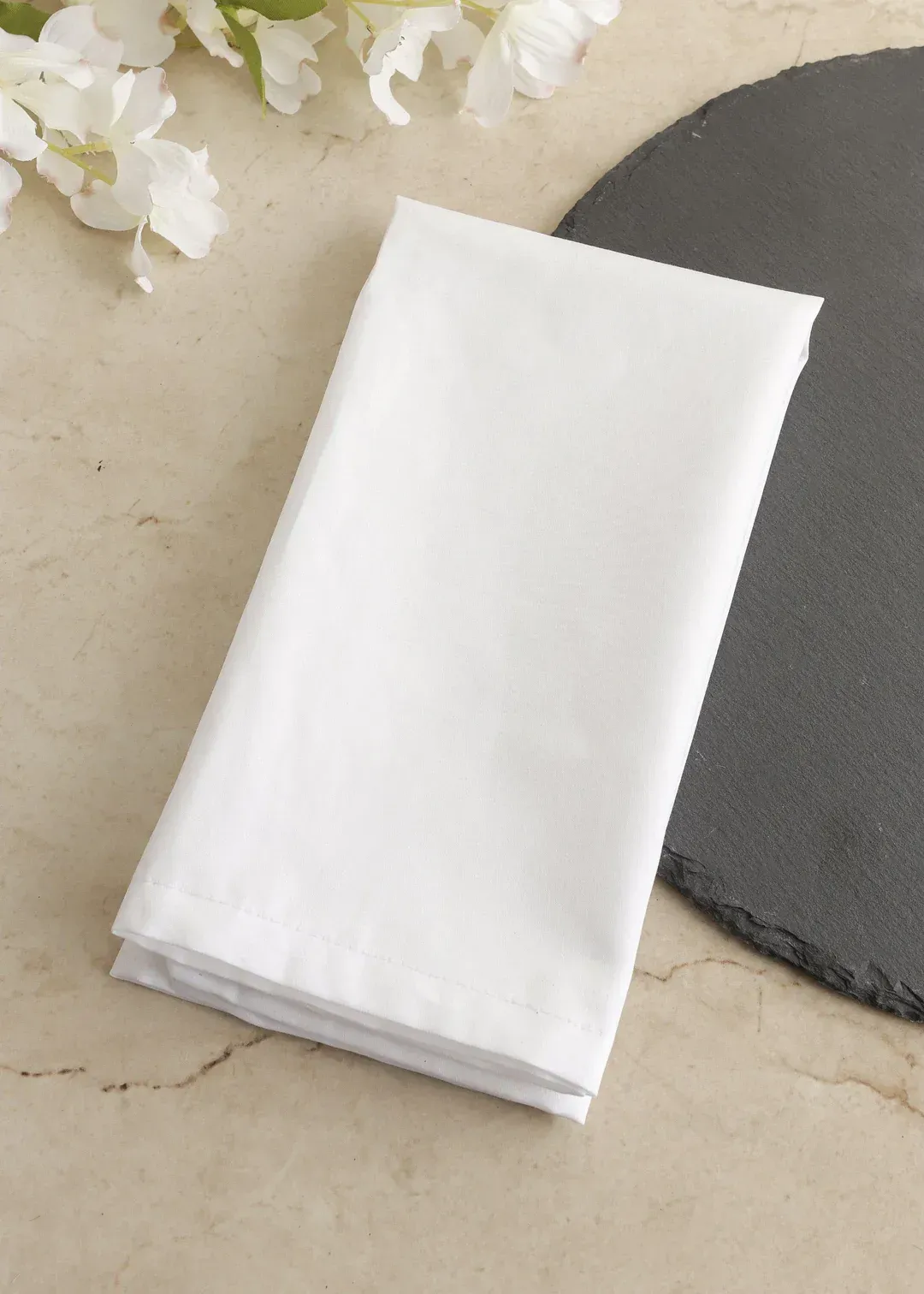 Una servilleta blanca está sobre una mesa al lado de flores.