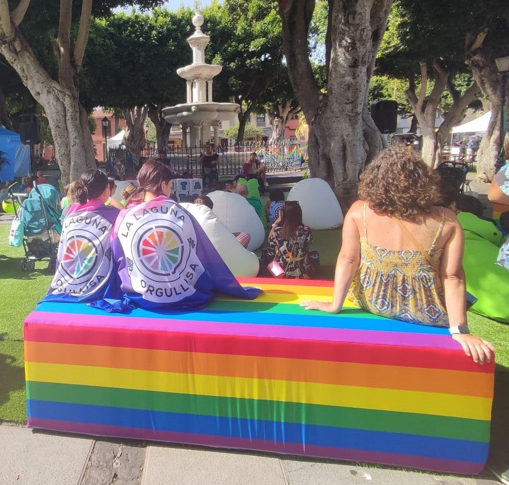 Un grupo de personas está sentado en un banco de colores del arco iris.
