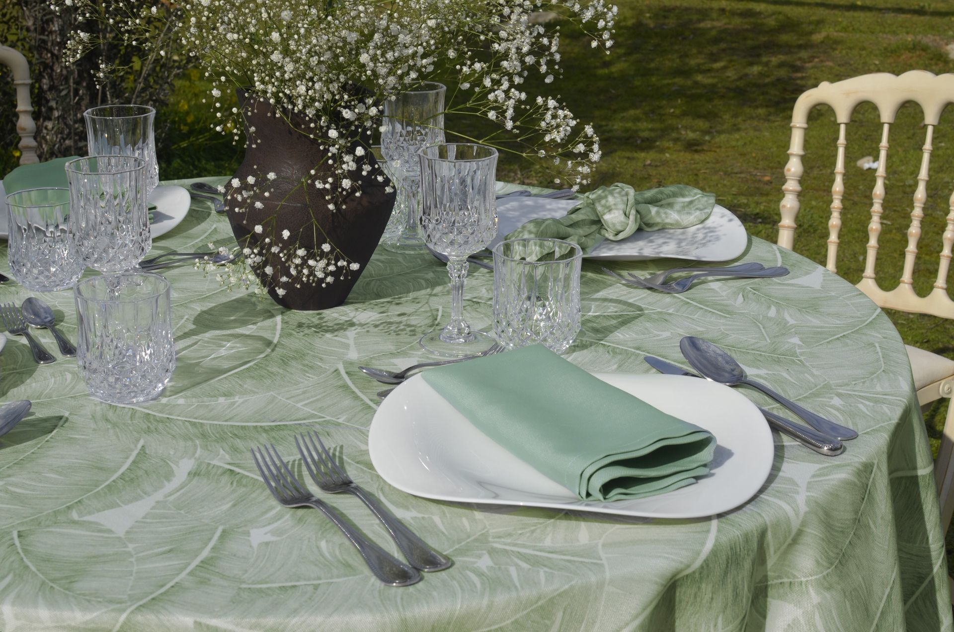 Juego de mesa para cenar al aire libre con mantel verde, servilletas y cristalería de cristal.