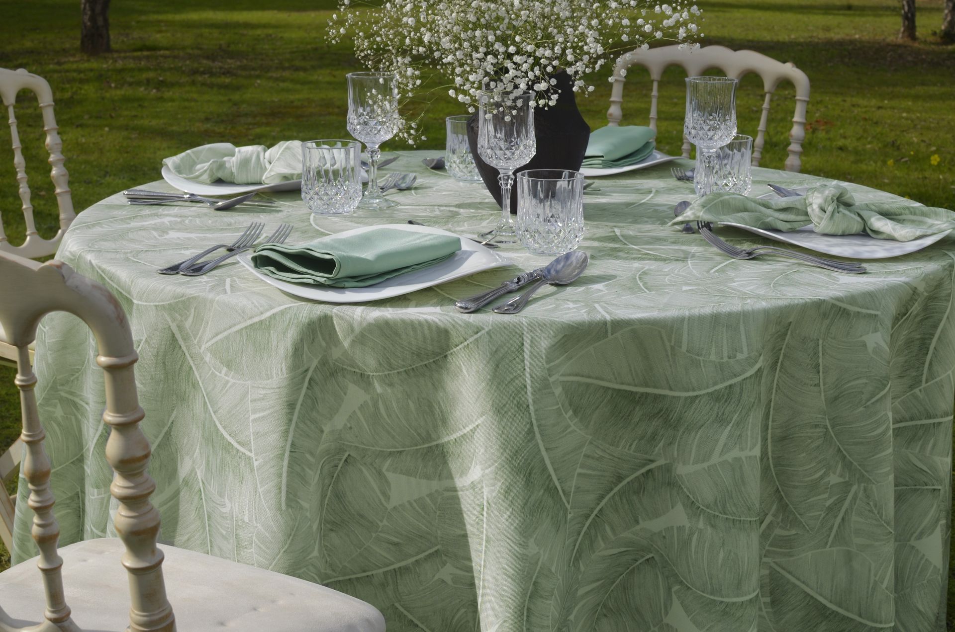 Conjunto de mesa redonda para evento al aire libre con mantel verde y elegantes cubiertos.