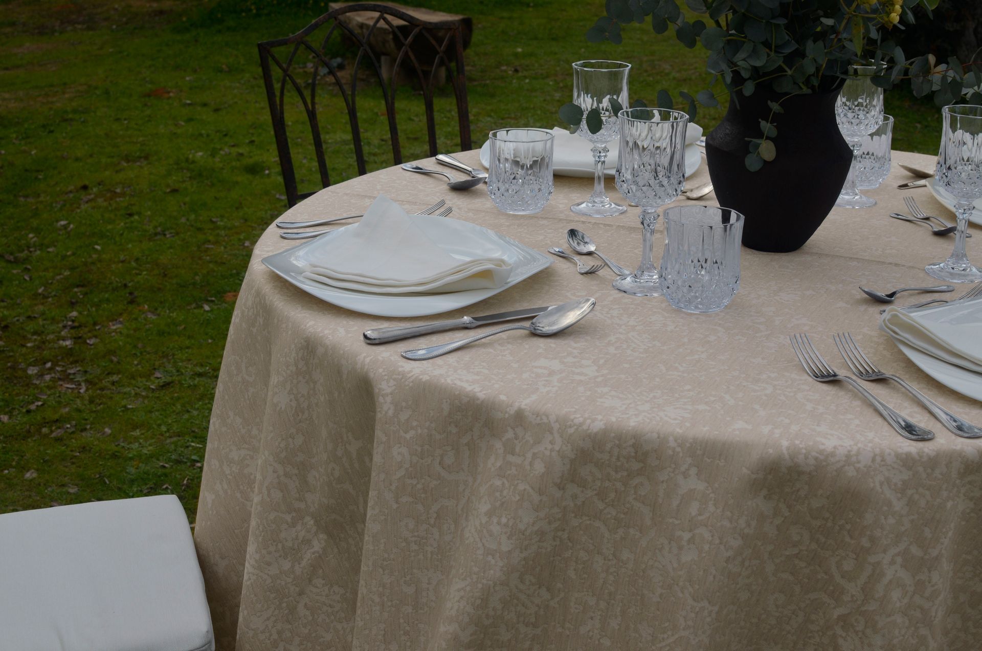 Una mesa puesta con platos, vasos, cubiertos y un jarrón con flores.