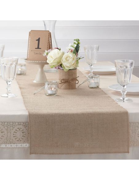 Decoración de mesa con camino de arpillera, flores, vasos y mesa número 1.