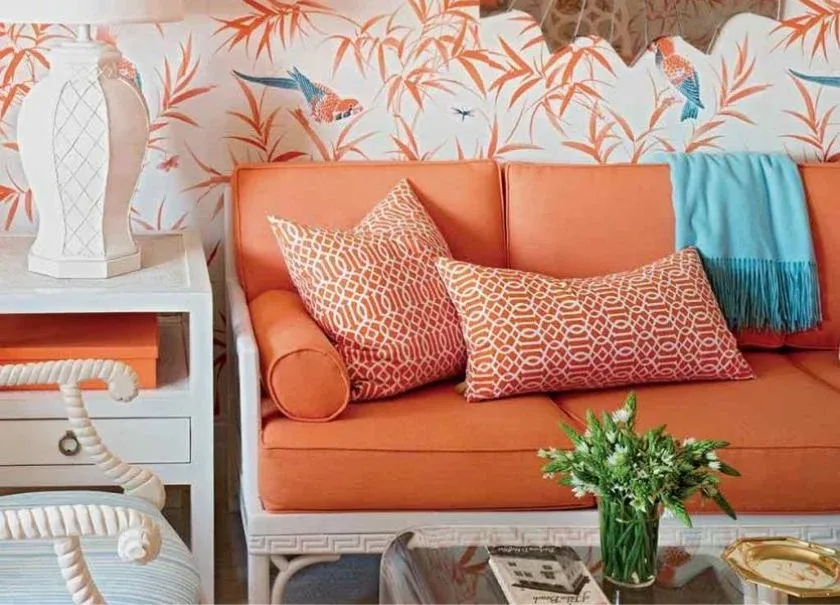 Una sala de estar con un sofá naranja y una mesita de noche blanca.