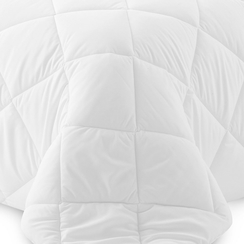 Un primer plano de un edredón blanco sobre una cama sobre un fondo blanco.