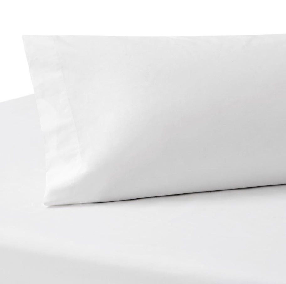 Una almohada blanca reposa sobre una colcha blanca.