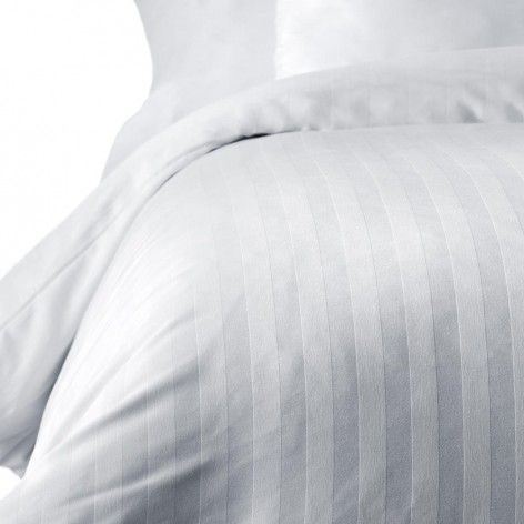 Una cama con un edredón blanco y almohadas encima.