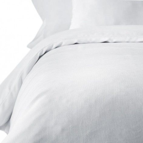 Un primer plano de un edredón blanco y almohadas en una cama.