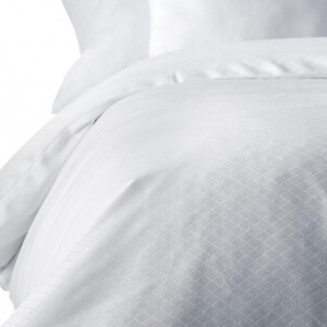 Un primer plano de un edredón blanco y almohadas en una cama.
