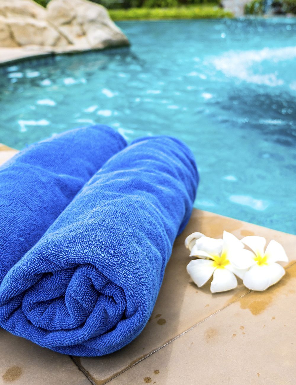 Dos toallas azules están enrolladas al lado de una piscina.