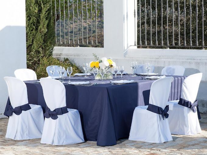 Una mesa con un mantel azul y sillas blancas.