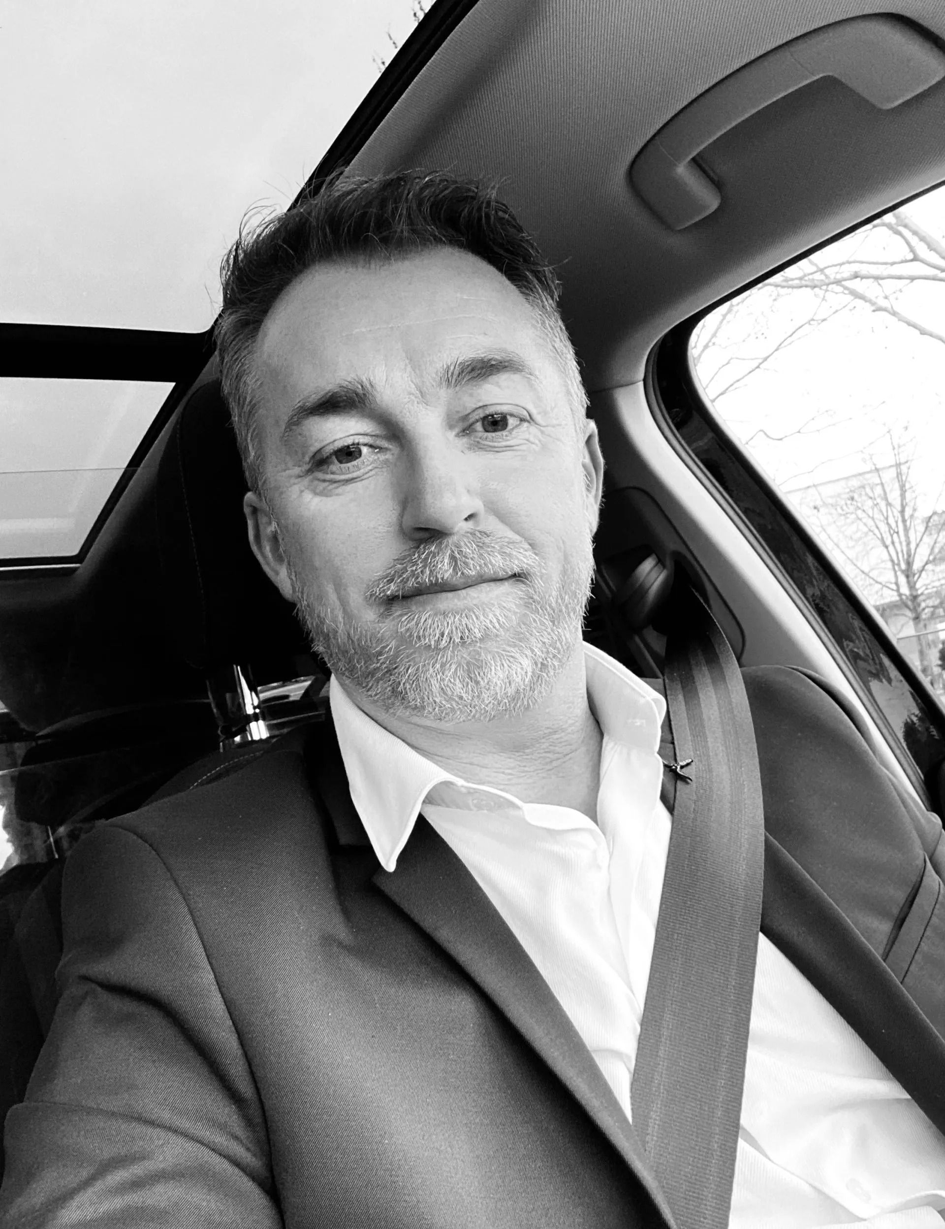 Un homme assis dans une voiture, portant une veste et une ceinture de sécurité.