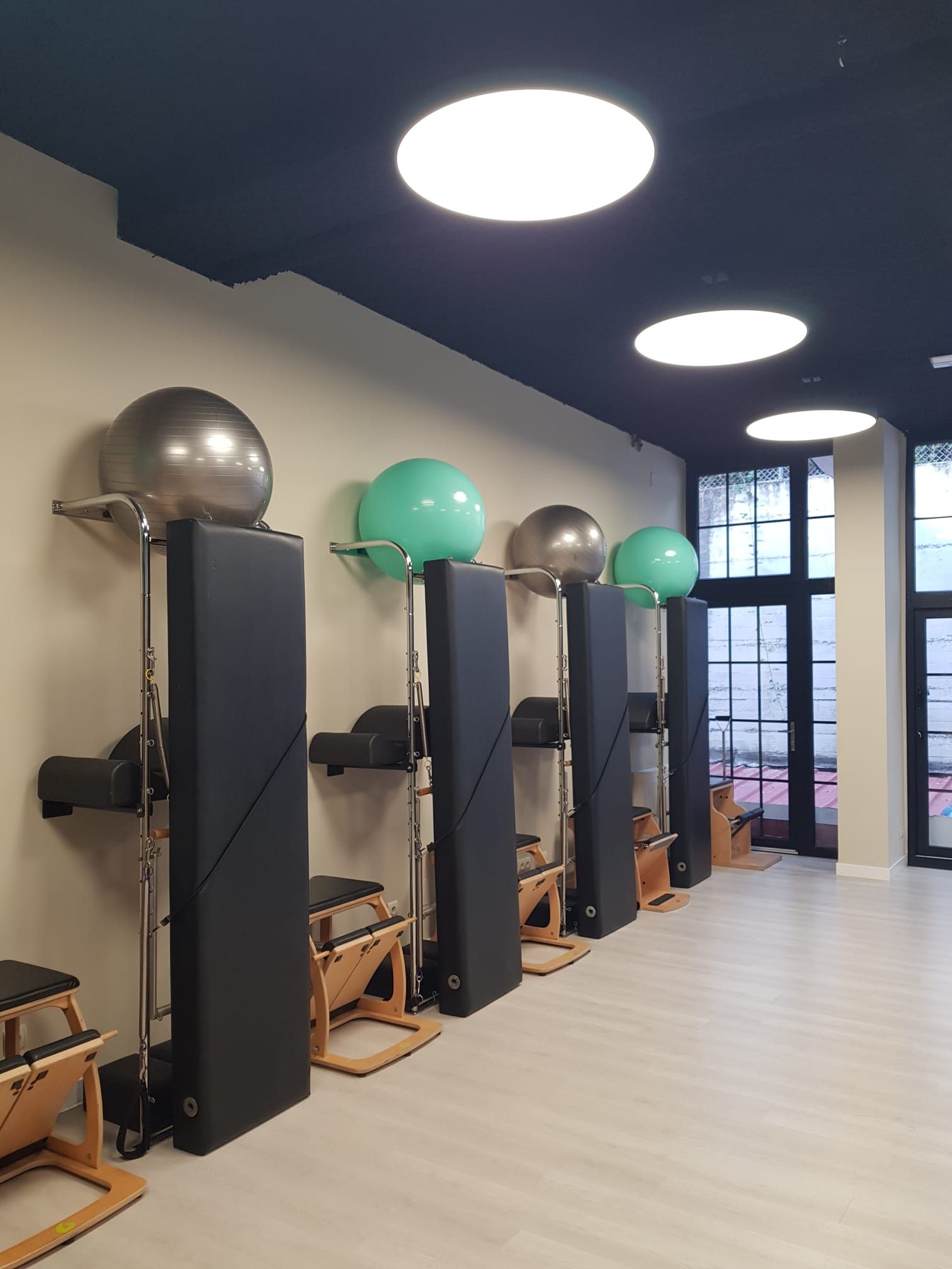 Estudio con máquinas de Pilates reformer, balones de estabilidad y grandes luces redondas en el techo.