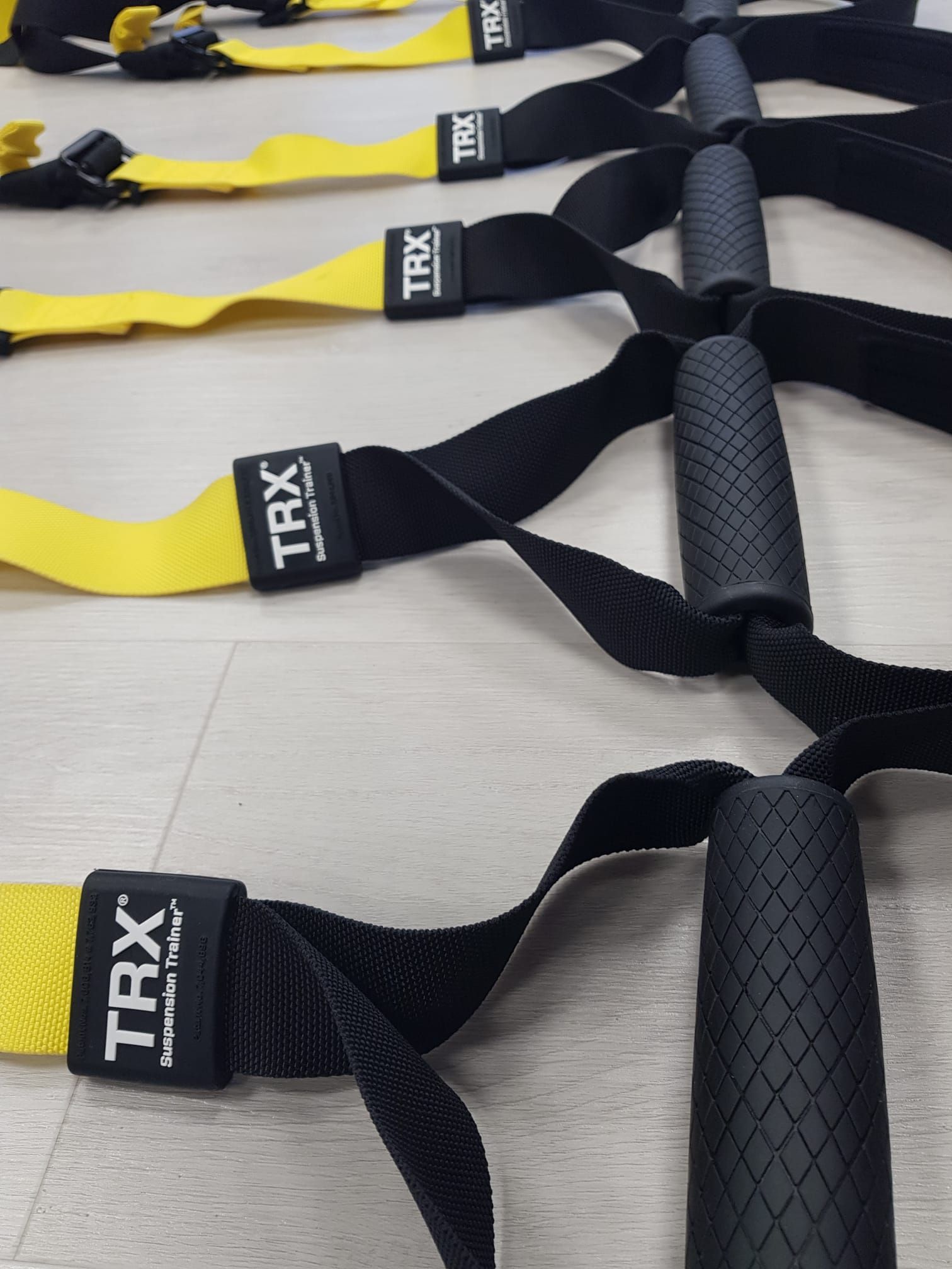 Correas de suspensión TRX alineadas sobre un suelo claro, asas negras y amarillas visibles