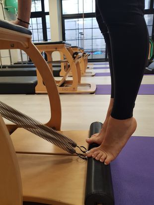 Una persona descalza presiona los dedos de los pies contra un rodillo de espuma negro en un estudio de Pilates.