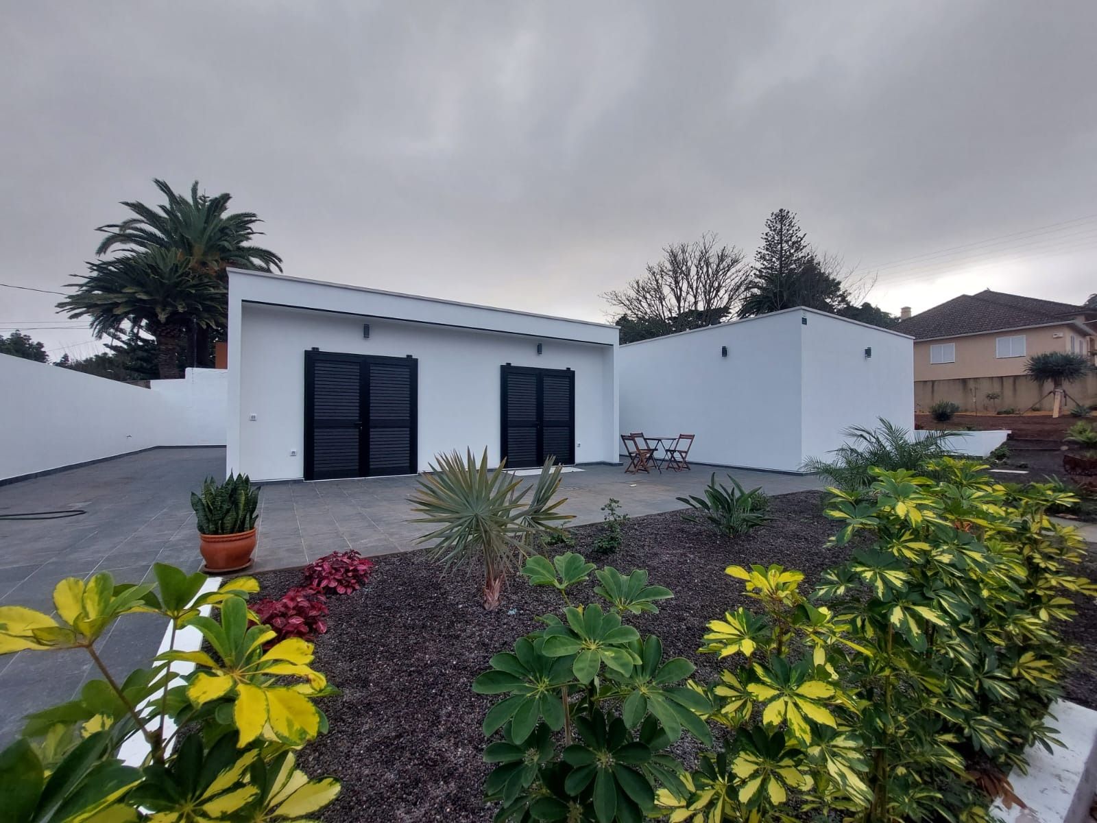 Una casa blanca con puertas negras está rodeada de plantas y arbustos.
