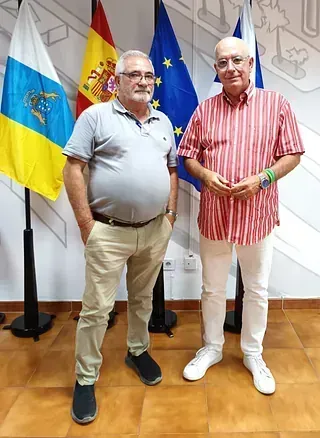 Dos hombres están parados uno al lado del otro frente a banderas.