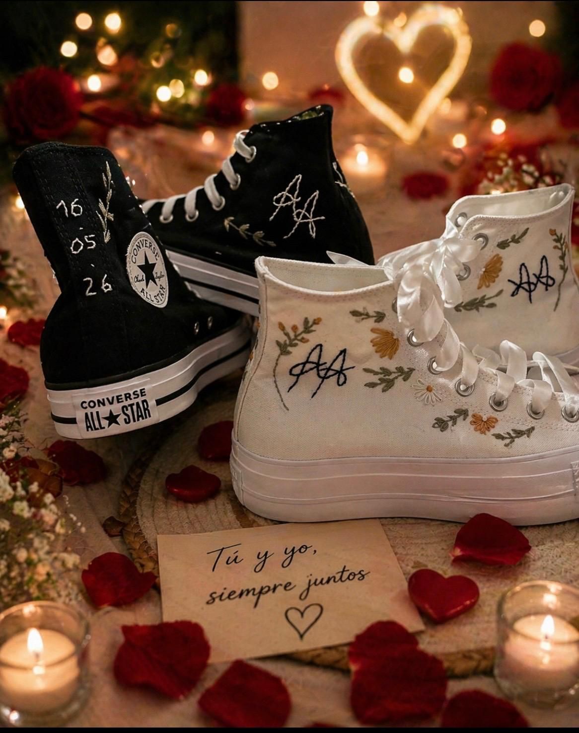 Zapatillas deportivas blancas y negras decoradas con diseños de corazones y flores, rodeadas de pétalos de rosa y velas.