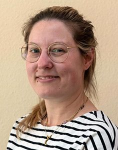 Eine Frau mit Brille und gestreiftem Hemd lächelt in die Kamera.