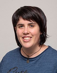 Eine Frau mit blauem Hemd und Halskette lächelt in die Kamera.