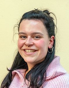 Eine Frau in einem rosa Pullover und Creolen lächelt in die Kamera.