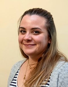 Eine Frau in einem gestreiften Hemd und einem grauen Pullover lächelt in die Kamera.