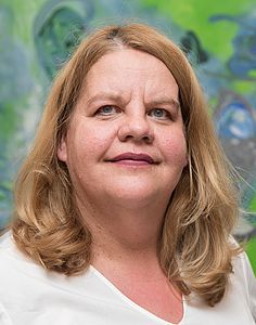 Eine Frau in einem weißen Hemd lächelt vor einem Gemälde.
