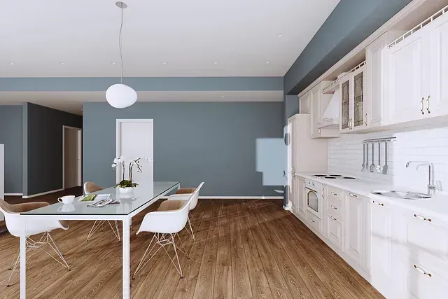 Cocina y comedor con pisos de madera, gabinetes blancos y una mesa de cristal con sillas blancas. Paredes azules por todas partes.