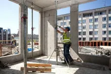 Un trabajador de la construcción ajusta los soportes de un muro de hormigón en una estructura parcialmente construida, con el horizonte de una ciudad de fondo.