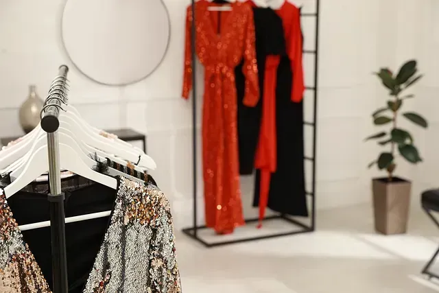 Vestidos colgados en percheros en una habitación luminosa. Entre los vestidos hay uno de lentejuelas y otros en naranja, negro y rojo.